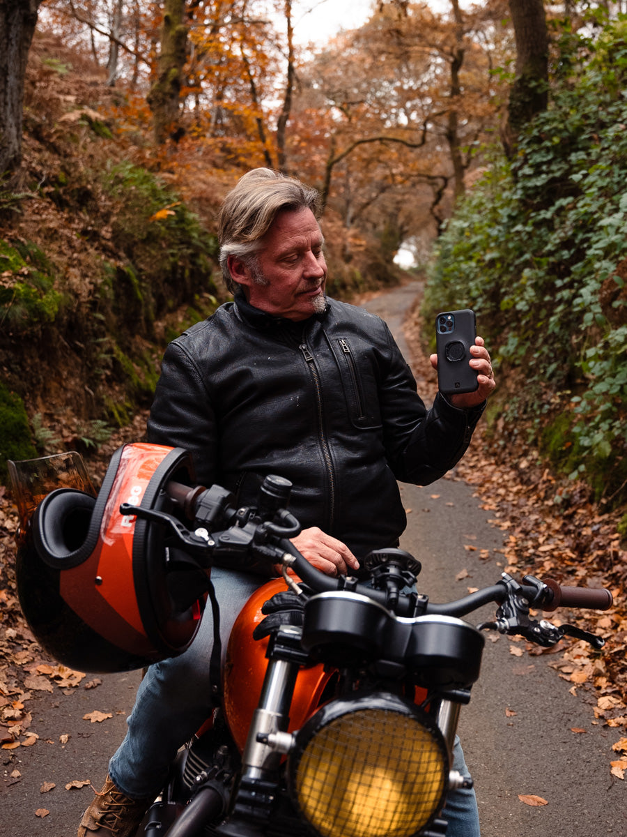 Photo of Charley Boorman on a motorbike with a phone in a Quad Lock case attached to a Weatherproof Wireless Charging Head attached to the handlebars of his bike